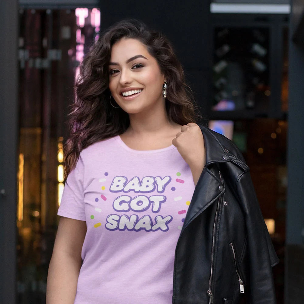 Person wearing a lilac BABY GOT SNAX t-shirt on a neon-lit street, leather jacket over shoulder