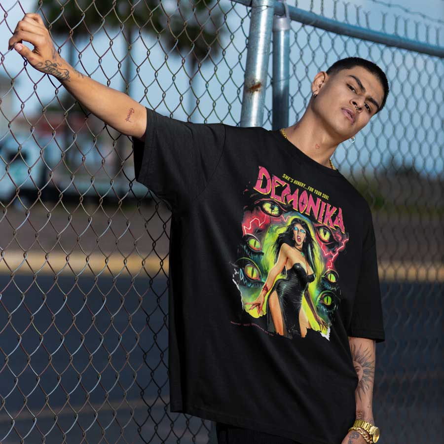 Person leaning on a chain-link fence in the black Demonika pulp horror tee