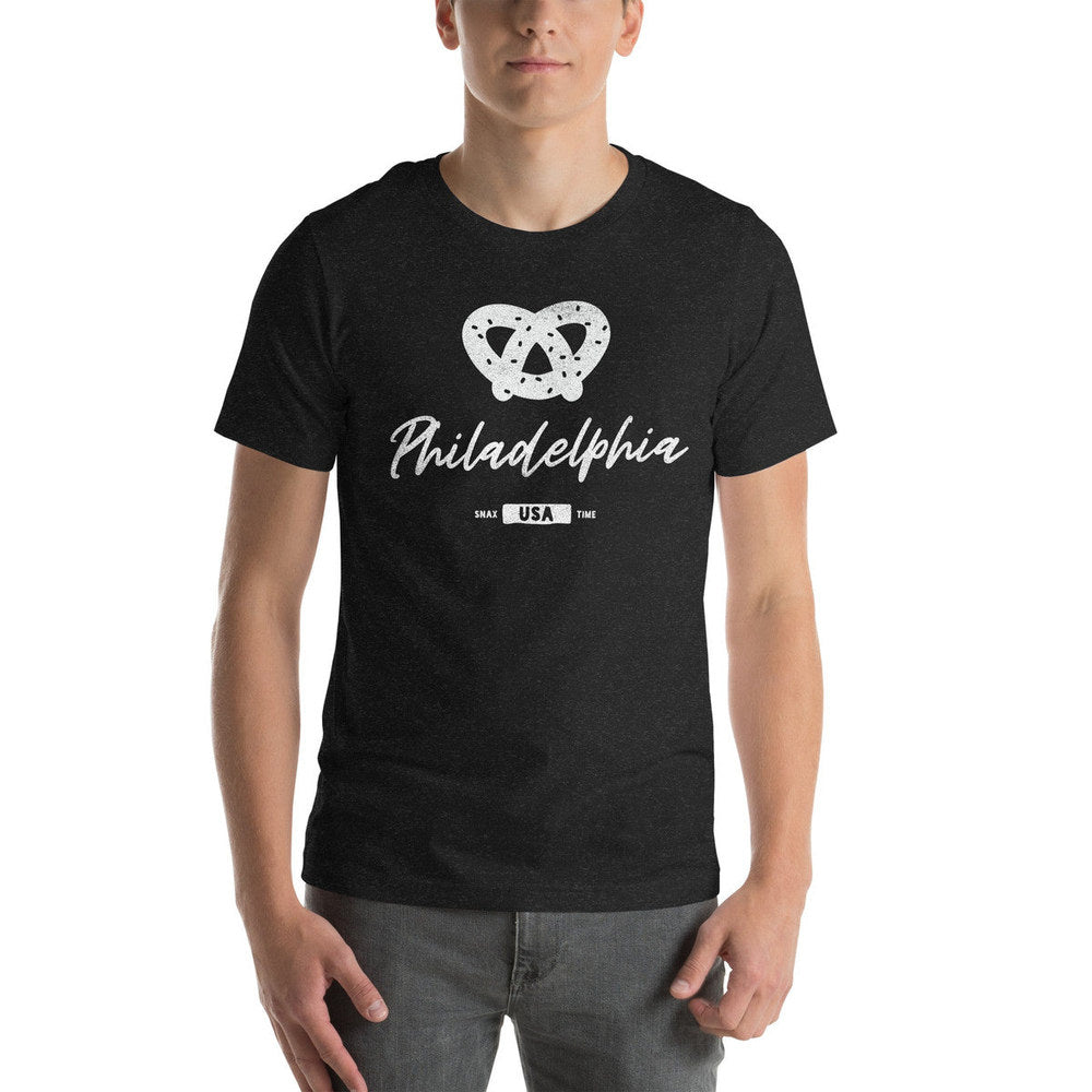 Person wearing a heather black t-shirt with a white soft pretzel and script "Philadelphia"