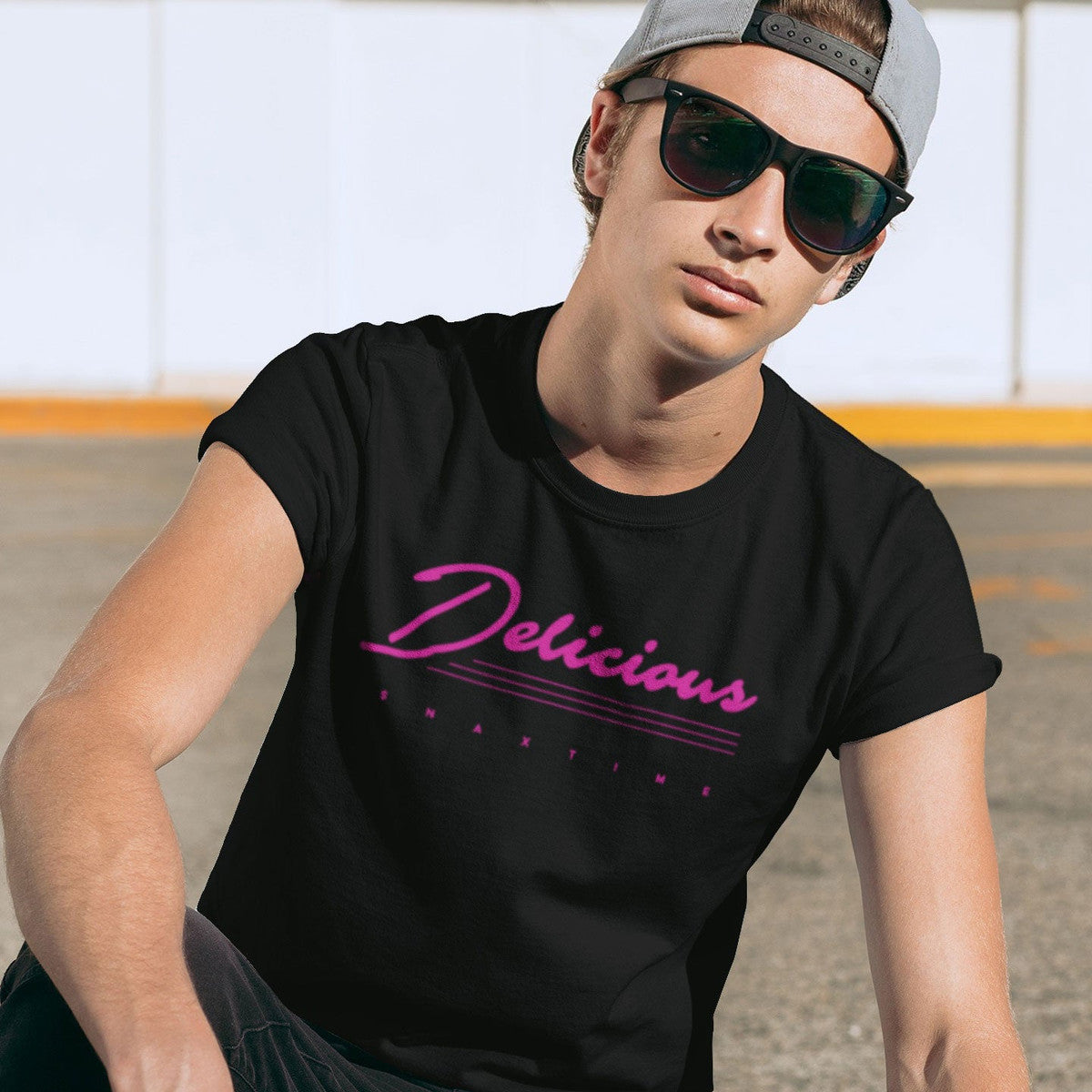 Man in sunglasses and a backwards cap wearing the black "Delicious" pink script t-shirt