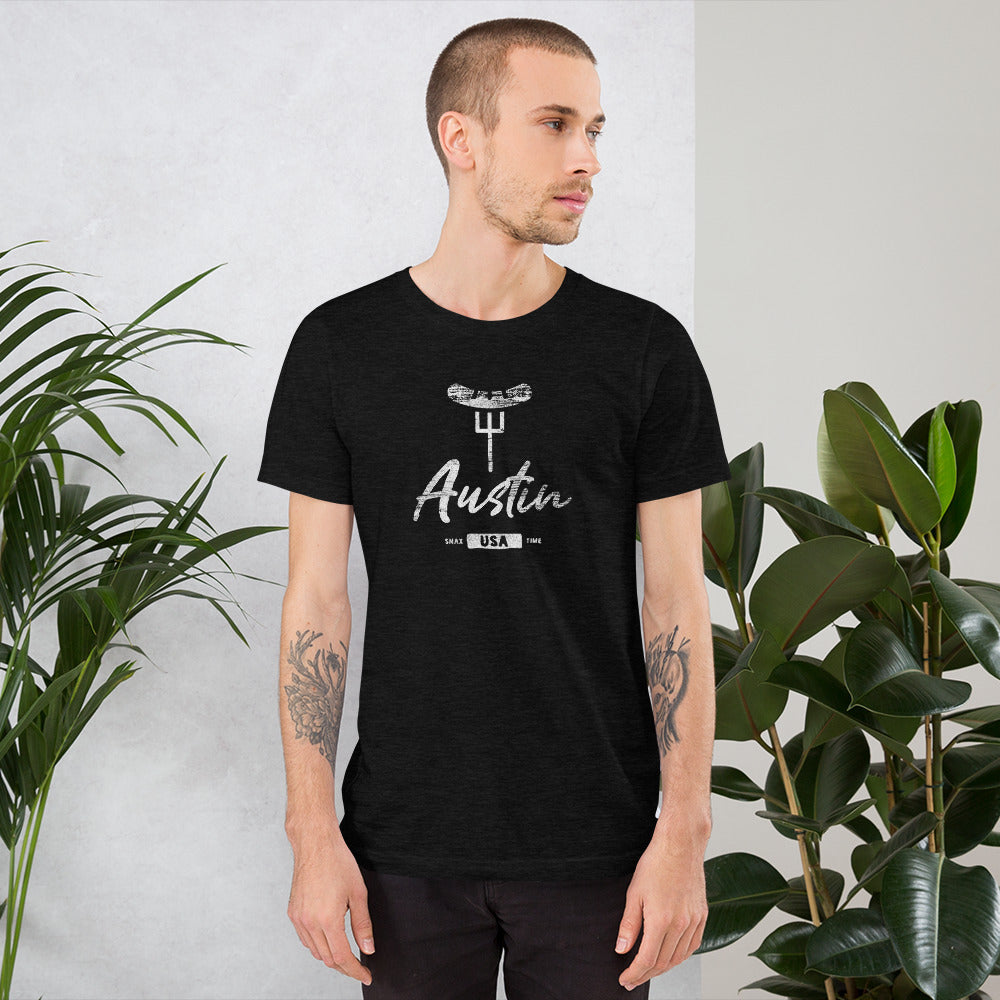 Man in a black heather "Austin" BBQ t-shirt standing between leafy houseplants