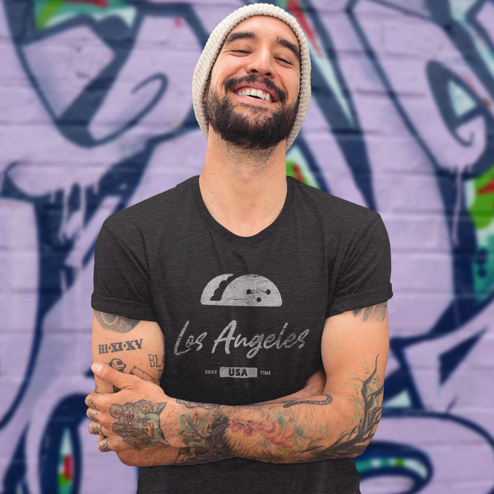 Smiling person in a beanie wearing a black heather Los Angeles taco tee by a graffiti wall
